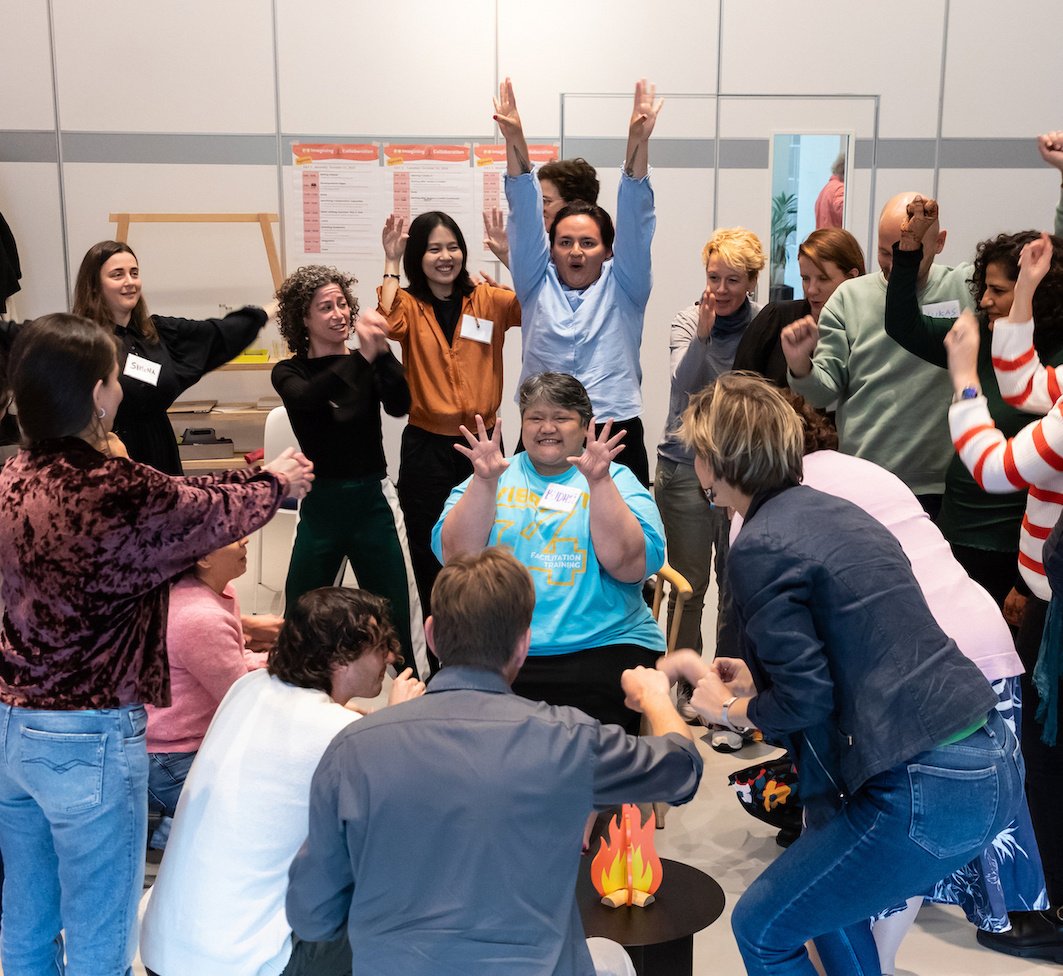 A group of collaboration participants stand around a facilitator in playful stances