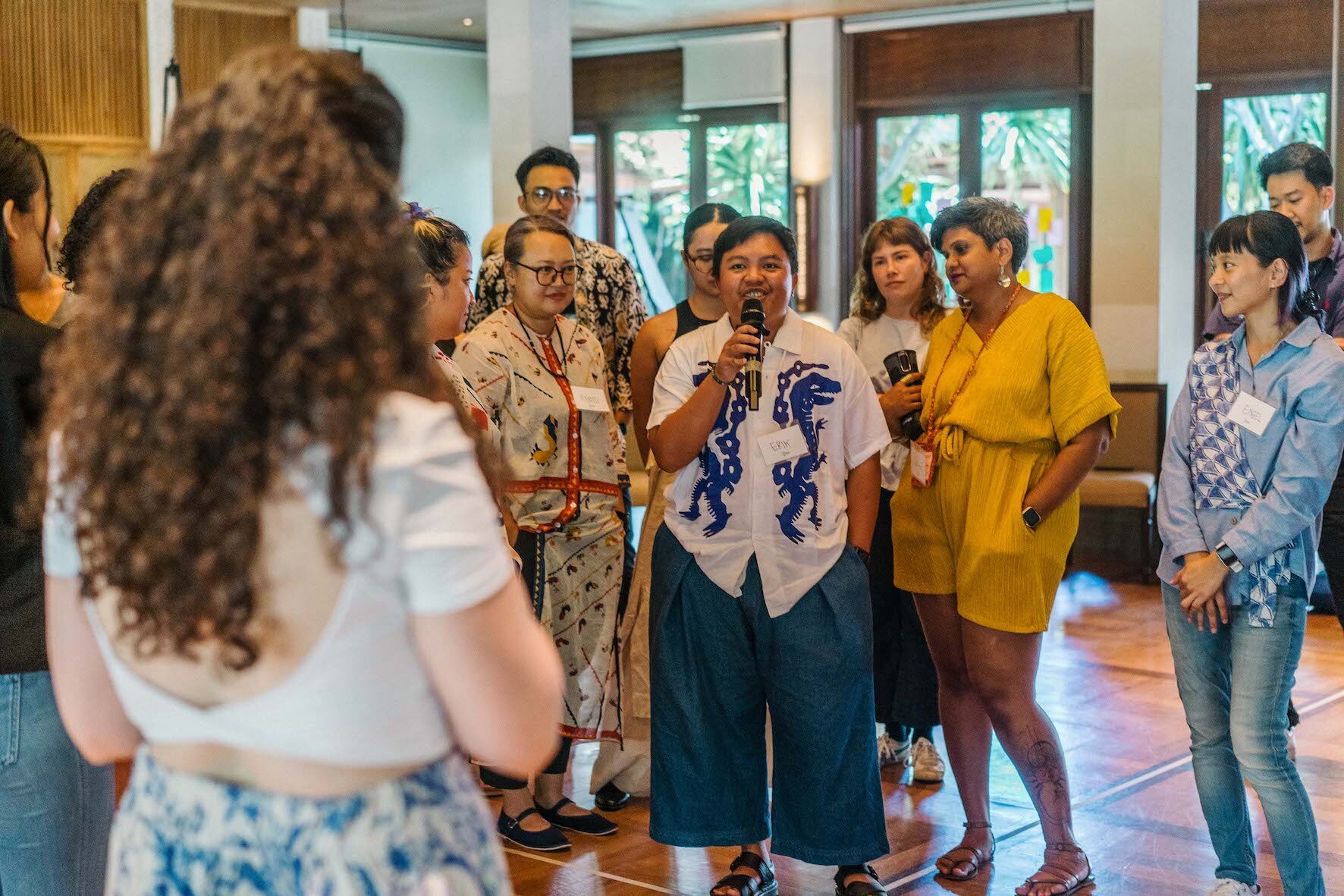 A group of people standing around a participant in a training who is speaking on a microphone