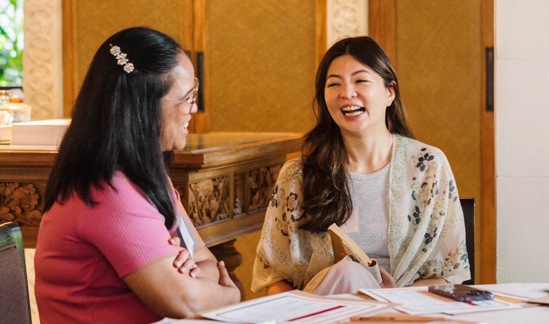 Two women smiling sitting at a table while talking to each other