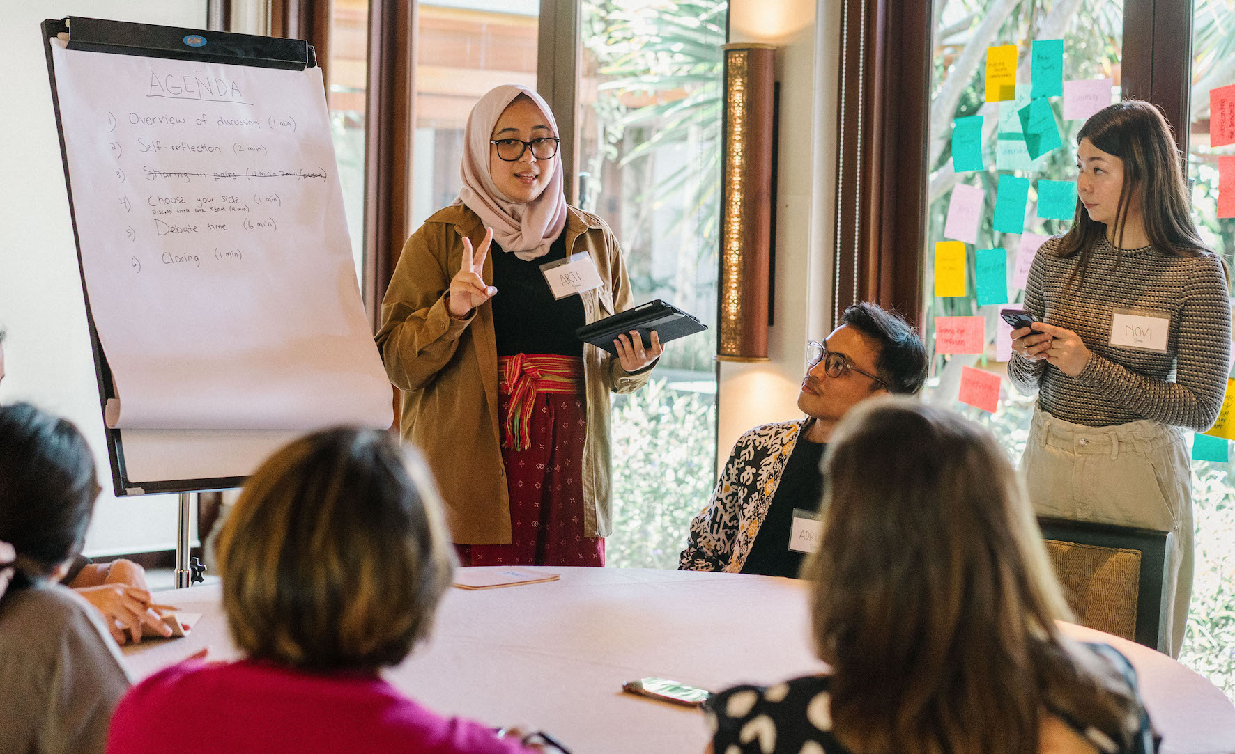 A woman facilitates a group conversation standing next to a flip chart